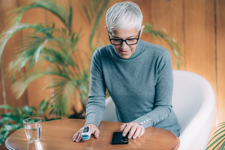 Woman Using Pulse Oximeter And Checking Readings On Phone